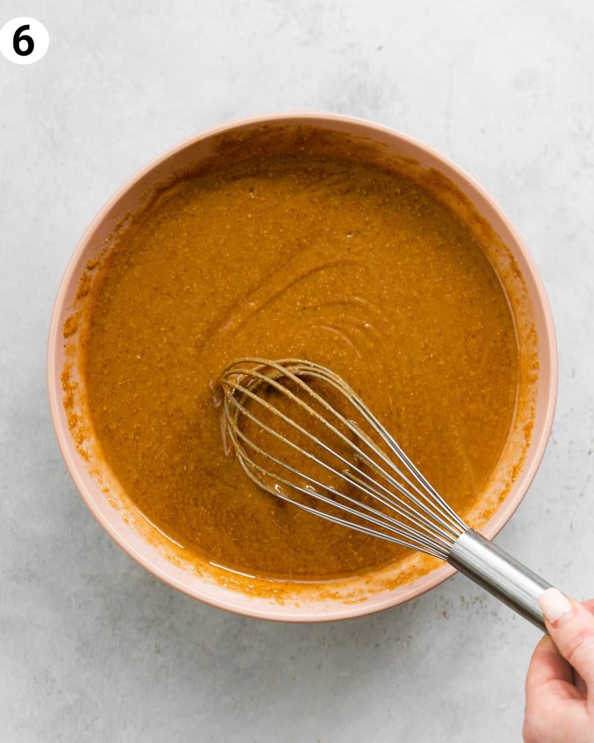 top down view of peanut butter caramel in a pink bowl with a whisk, on a grey surface.