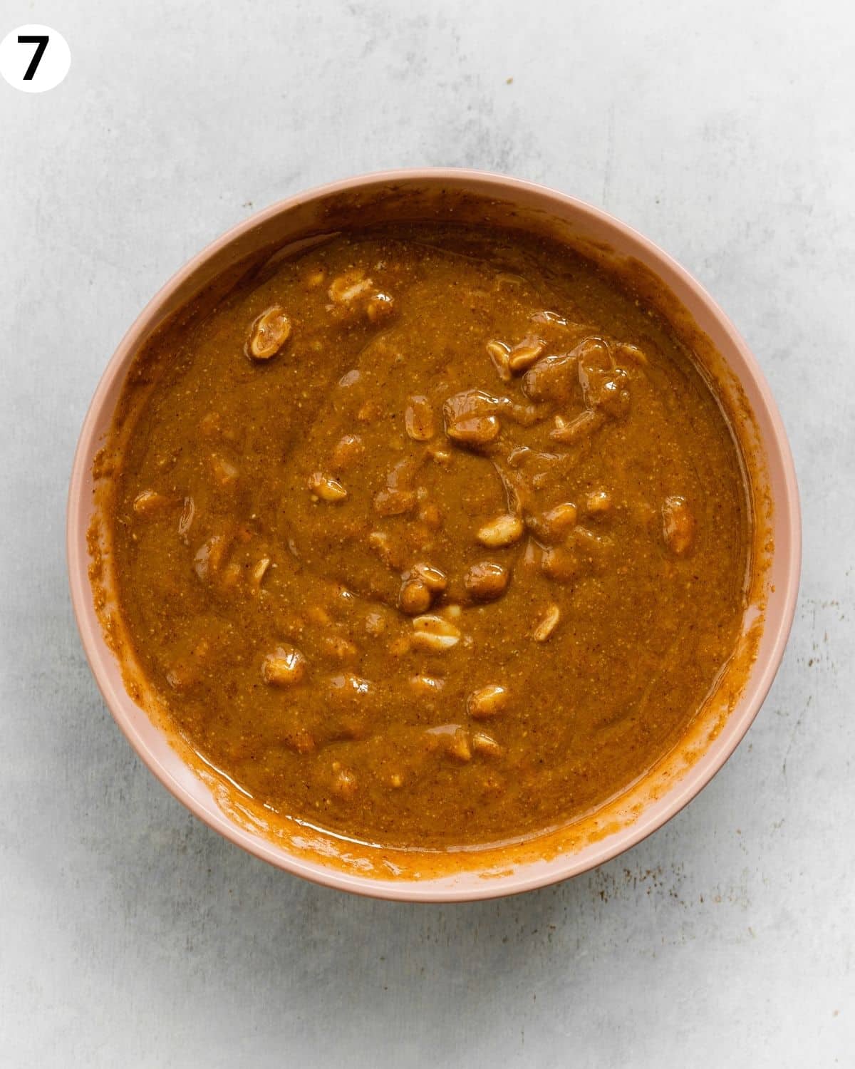 top down view of peanut butter caramel with peanuts in a pink bowl on top of a grey surface.