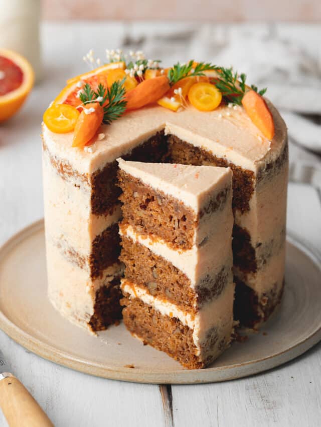 layered vegan carrot cake with orange cream cheese frosting on a plate.
