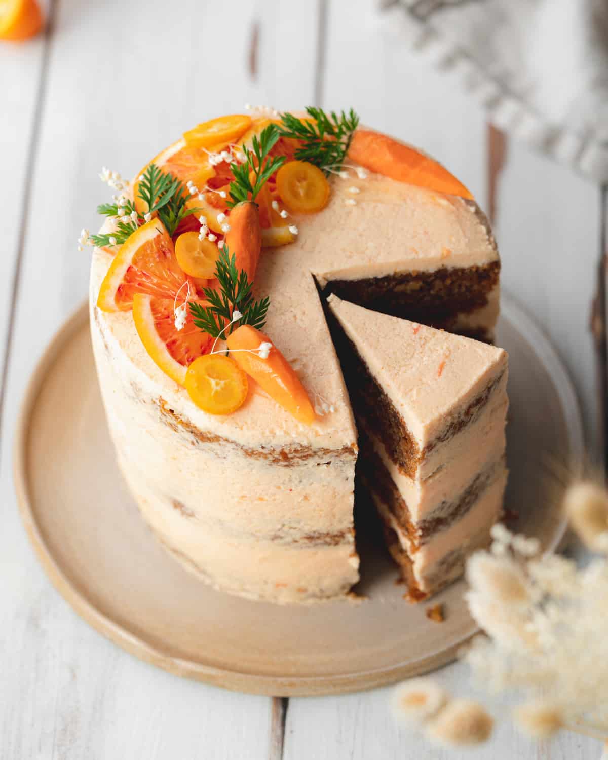 carrot cake with blood oranges and mini carrots on a white wooden surface.