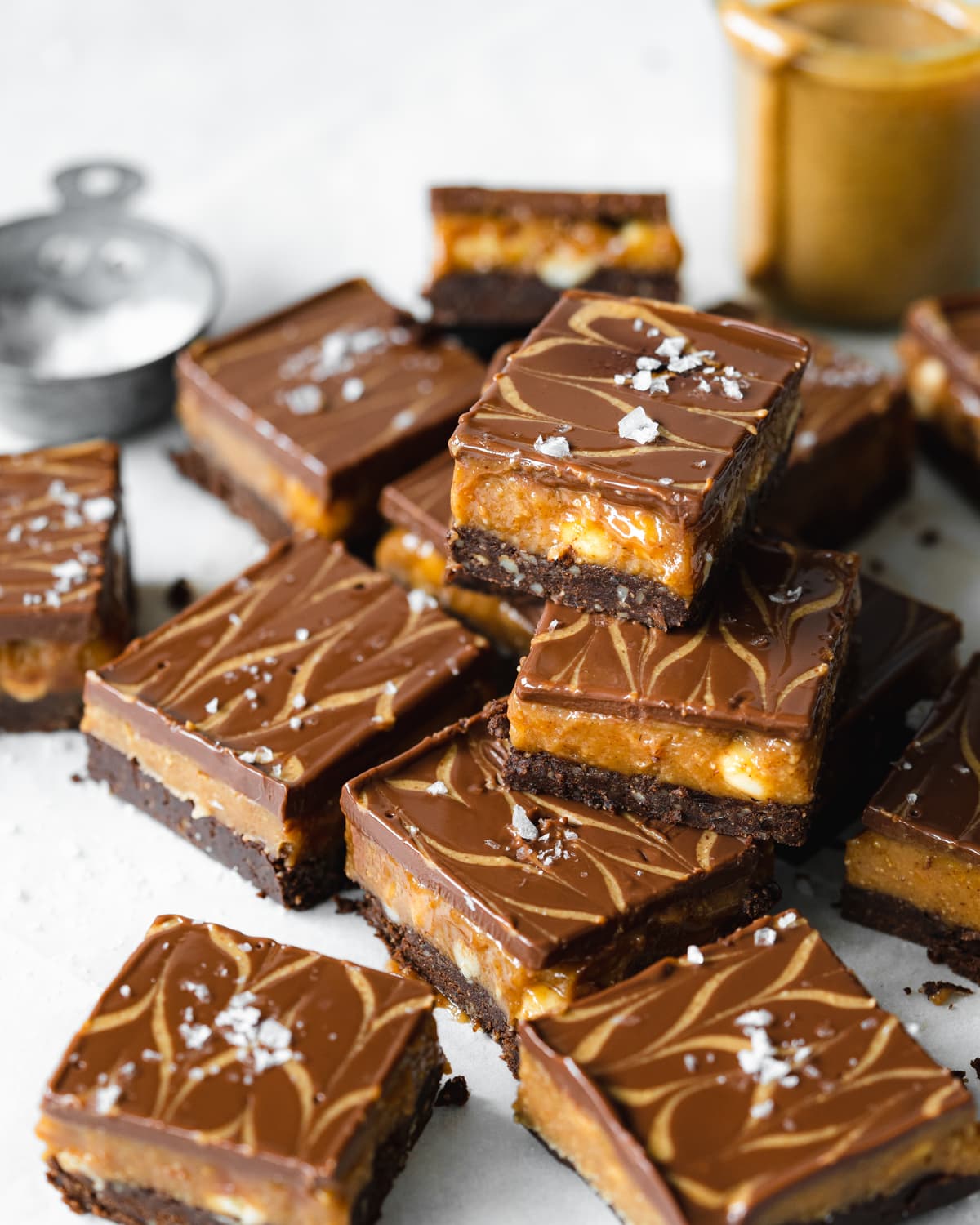 no bake brownies with a layer of peanut butter and chocolate stacked on top of each other, with a jar of peanut butter and salt in the background.