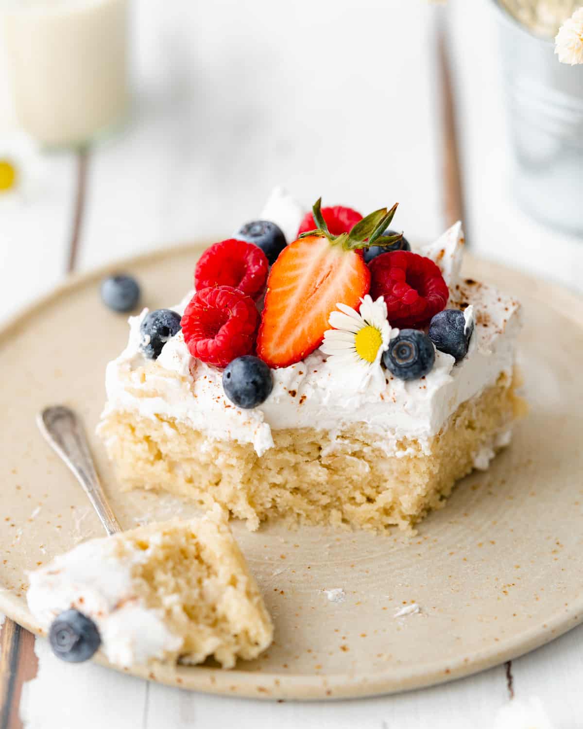 slice of tres leche cake on a ceramic plate with fresh blueberries, strawberries and raspberries on top.