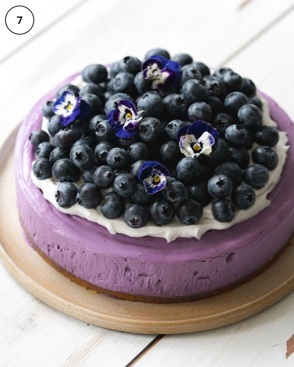 blueberry cheesecake on a ceramic plate with cream and fresh blueberries on top.