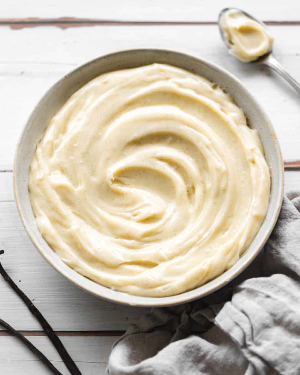 custard in a bowl with a spoon and vanilla pods scattered around it.