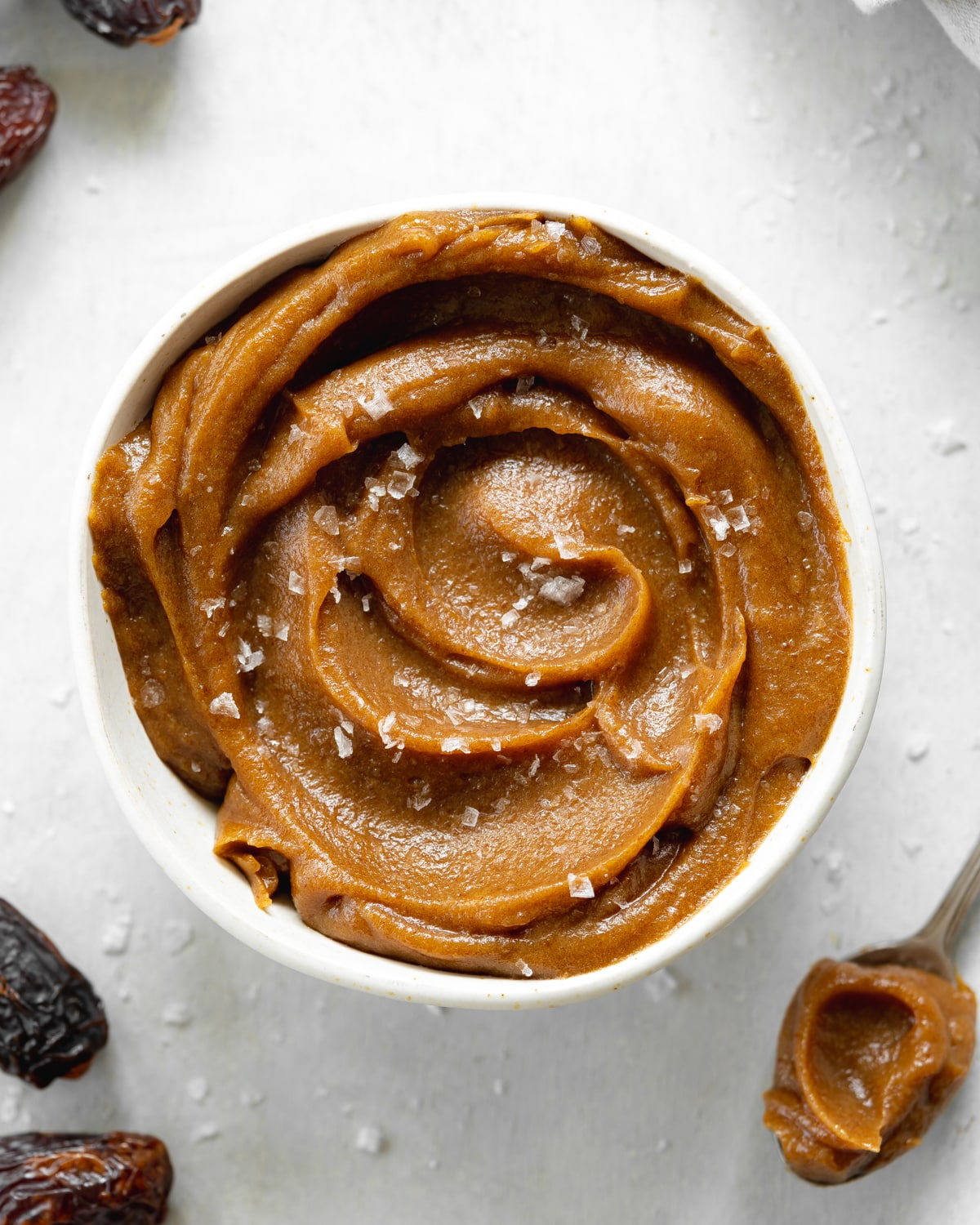 bowl of date caramel with flaky sea salt on top and dates scattered around it.