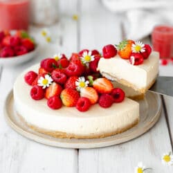 vanilla cheesecake on a plate with fresh raspberries, strawberries, and daisies on top.