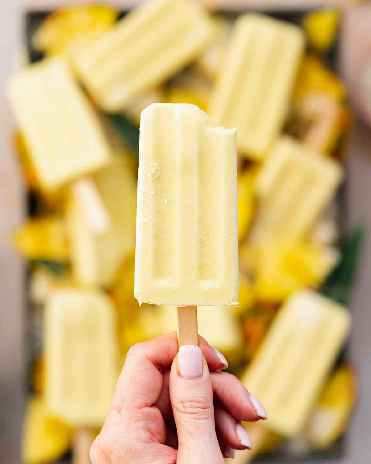 hand holding up a coconut pineapple popsicles with more popsicles in the background.