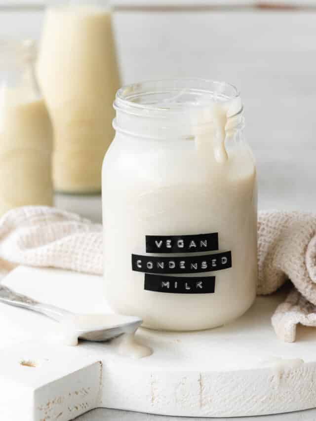a labelled jar of vegan sweetened condensed milk on a white wooden tray with milk bottles in the background.