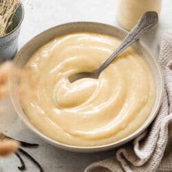 bowl of vegan custard with a spoon and cream flowers and a scrunched up towel around it.
