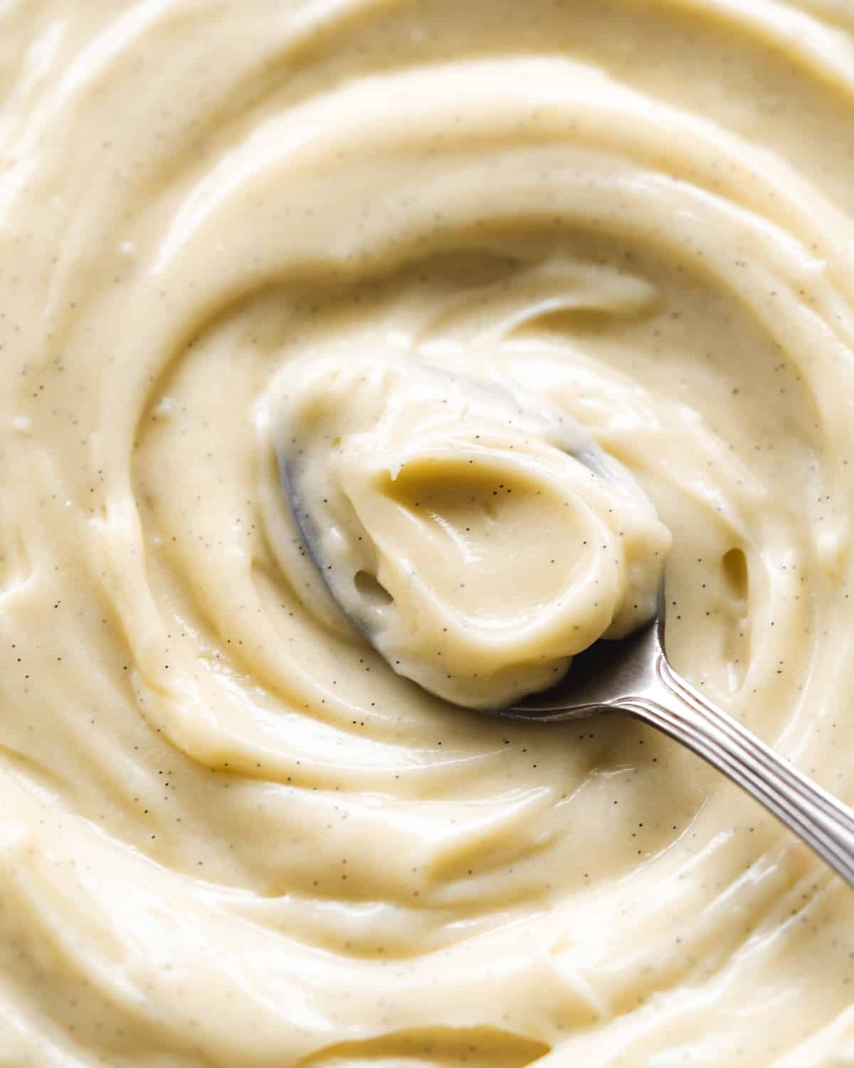close up of pastry cream with vanilla specks and a spoon inside.