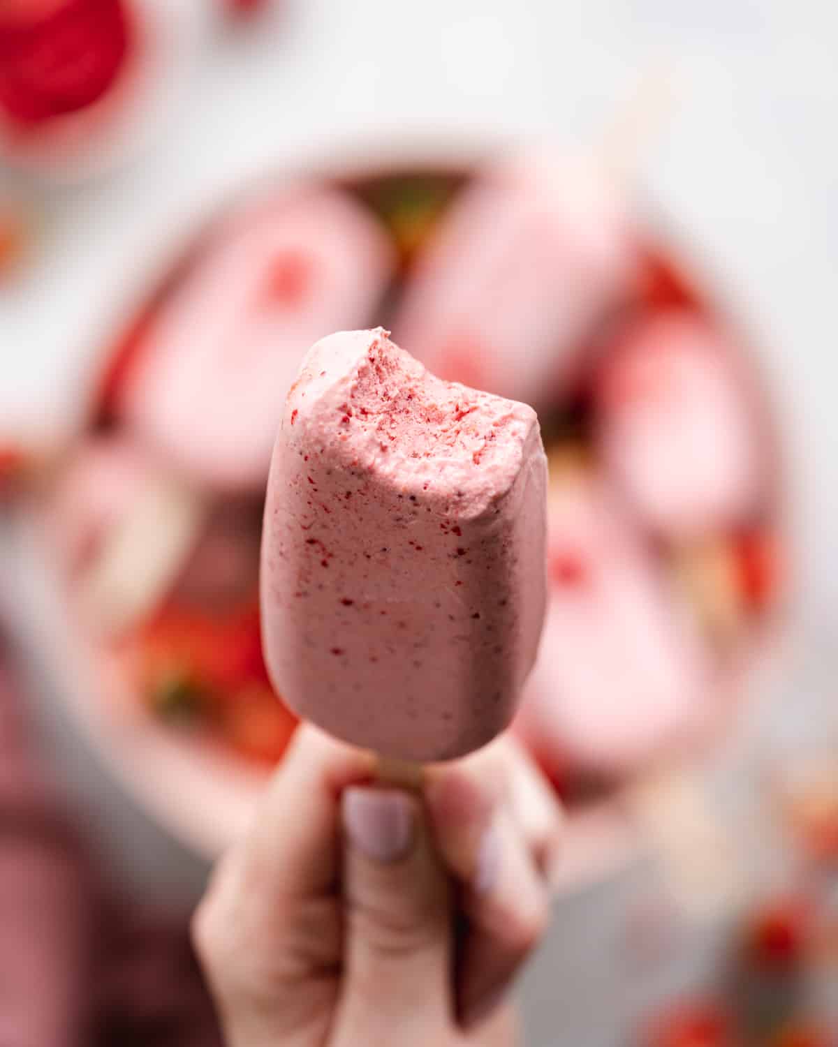 hand holding up a creamy strawberry ice cream bar.