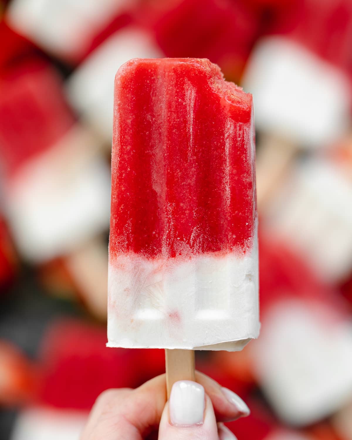 hand holding up a strawberry and yogurt popsicle.