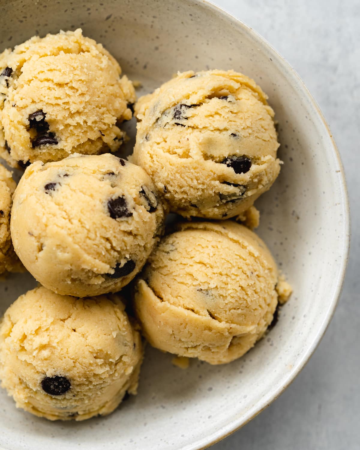 scoops of raw cookie dough in a grey ceramic bowl.