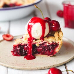 slice of vegan cherry pie with vanilla ice cream and cherry sauce on a ceramic plate.
