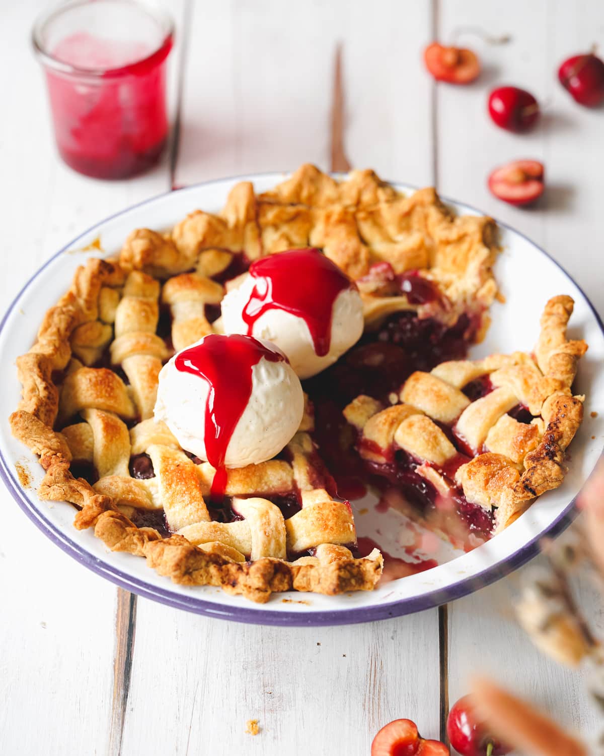 vegan cherry pie with vanilla ice cream and cherry sauce on a white wooden surface.