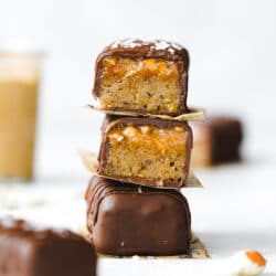 stack of chocolate peanut butter caramel bars with a jar of peanut butter in the background.