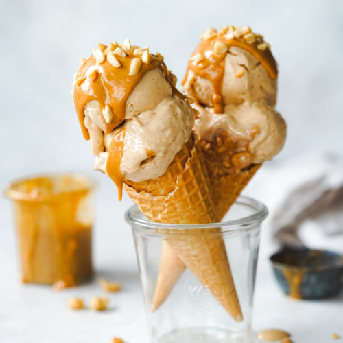 two ice cream cones with peanut butter ice cream in a glass jar with a small jar of peanut butter in the background.