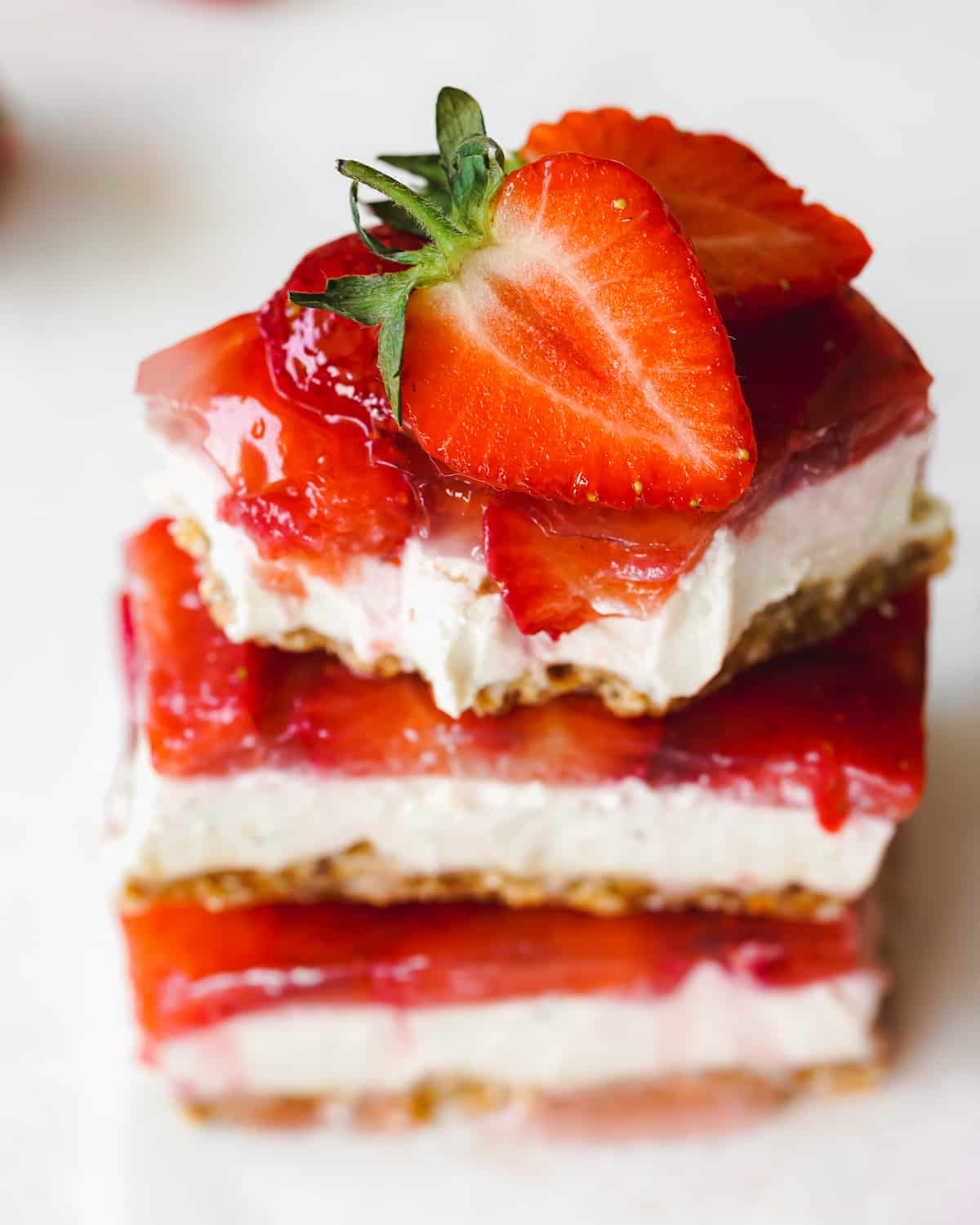 stack of vegan strawberry cheesecake bars with fresh strawberries on top.