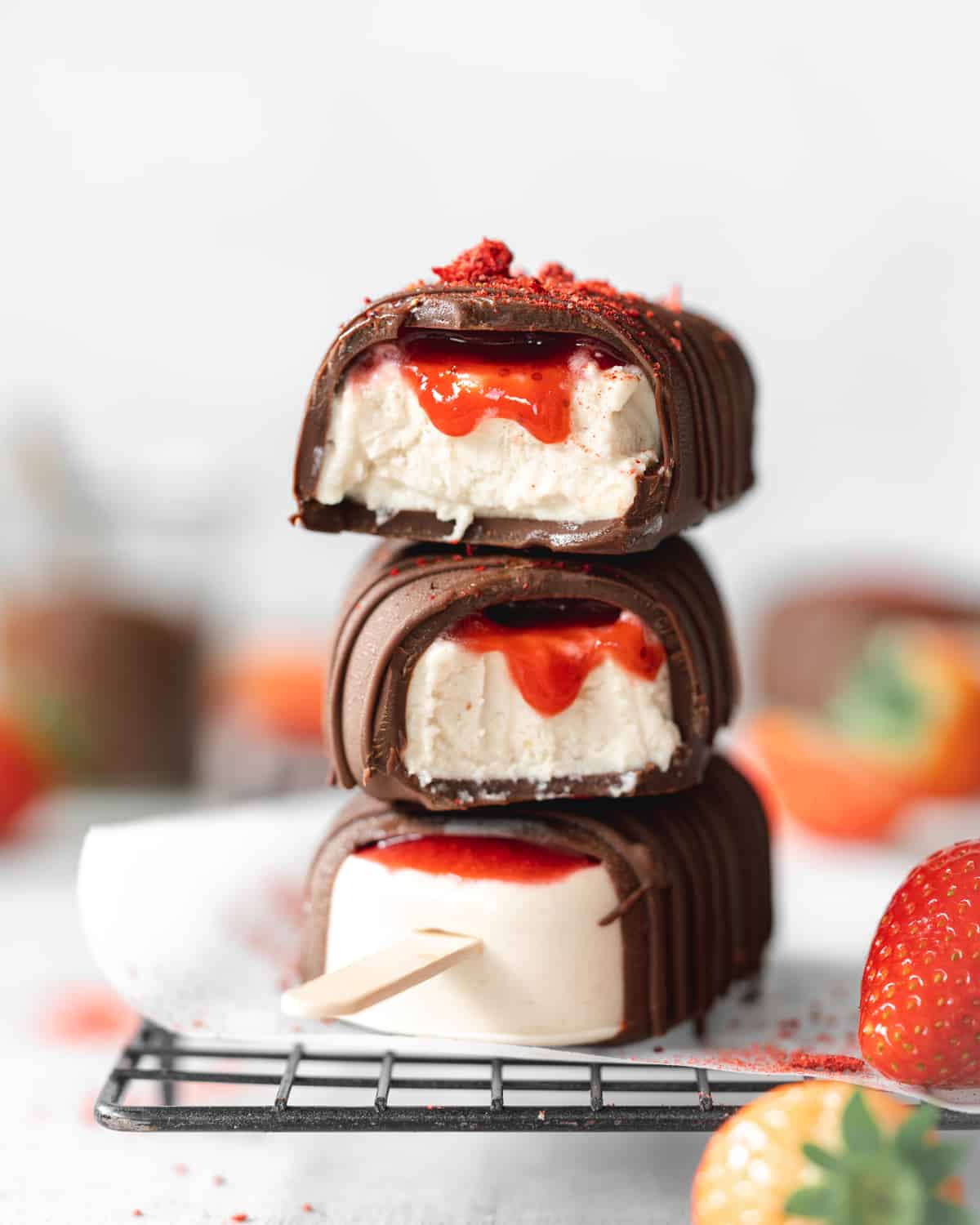 stack of vegan magnum ice cream bars with strawberry sauce on a cooling rack.