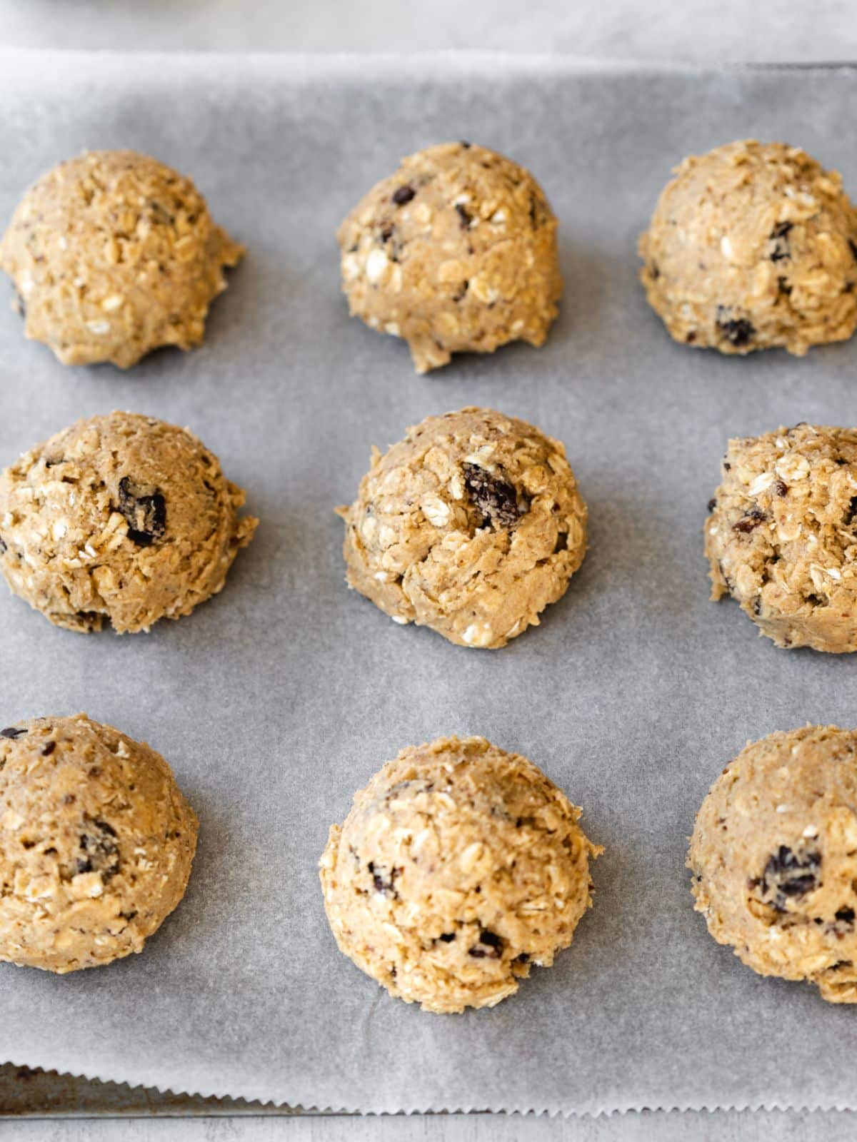 oatmeal raisin cookie dough balls measured out on a lined baking sheet.