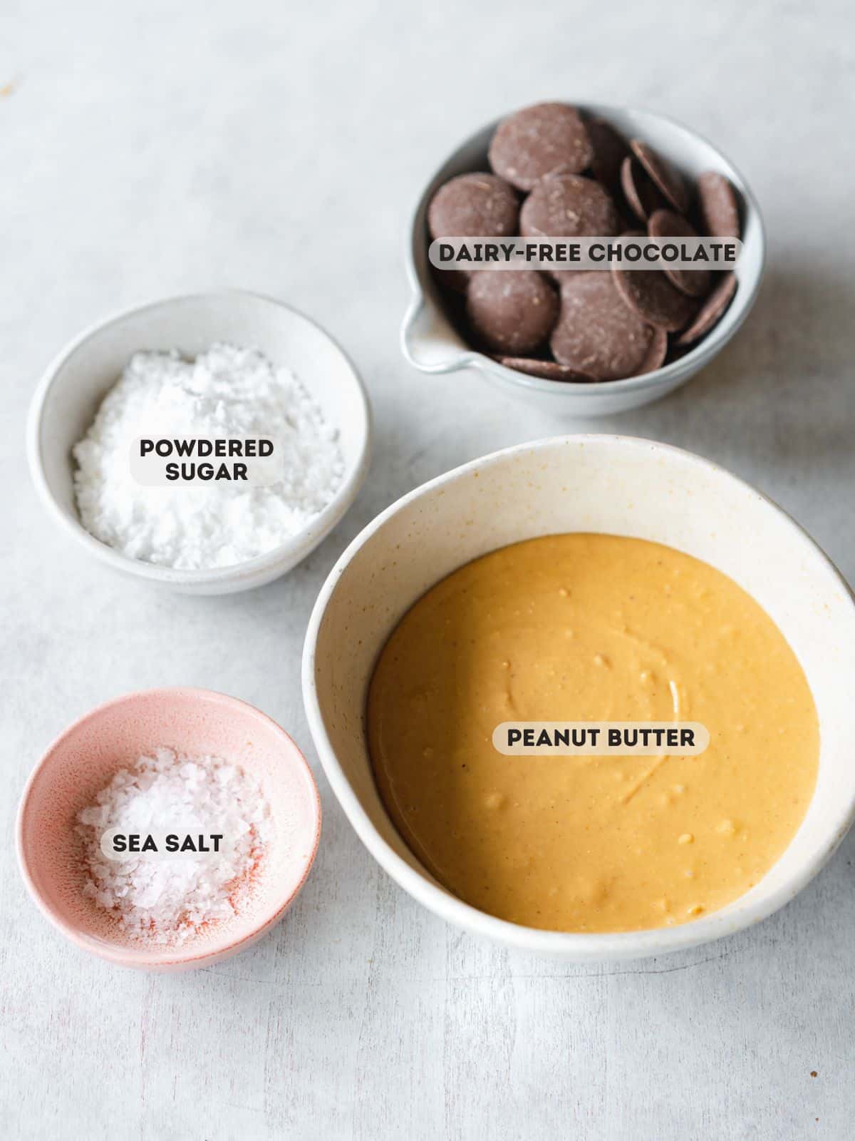 ingredients for homemade peanut butter cups measured out in bowls on a gray surface.