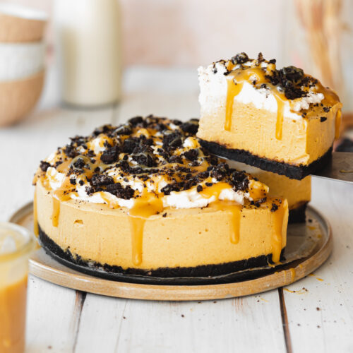 pumpkin cheesecake with crushed oreos and caramel sauce on top on a white wooden surface.