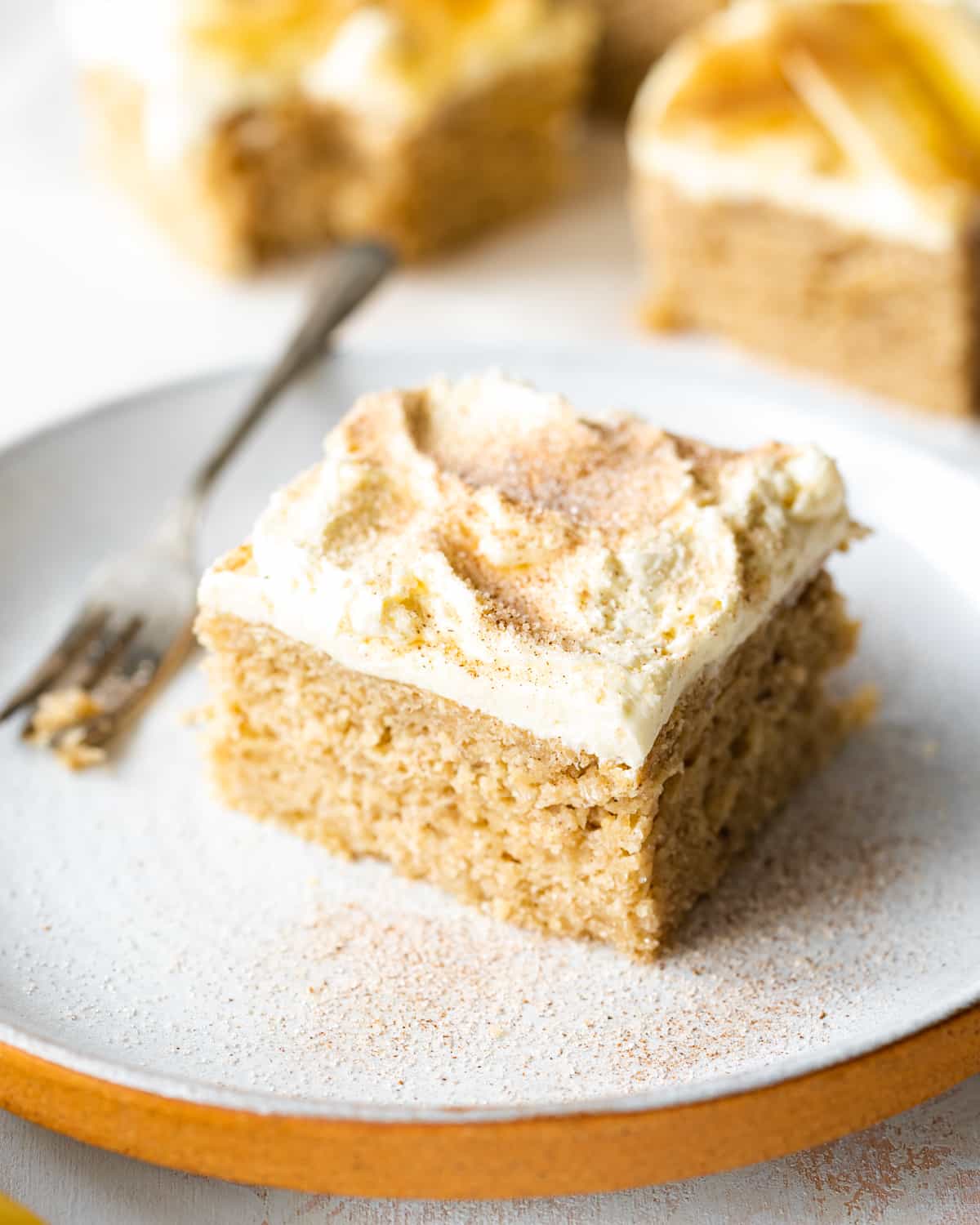 slice of banana cake with cream cheese frosting and cinnamon on a ceramic plate.