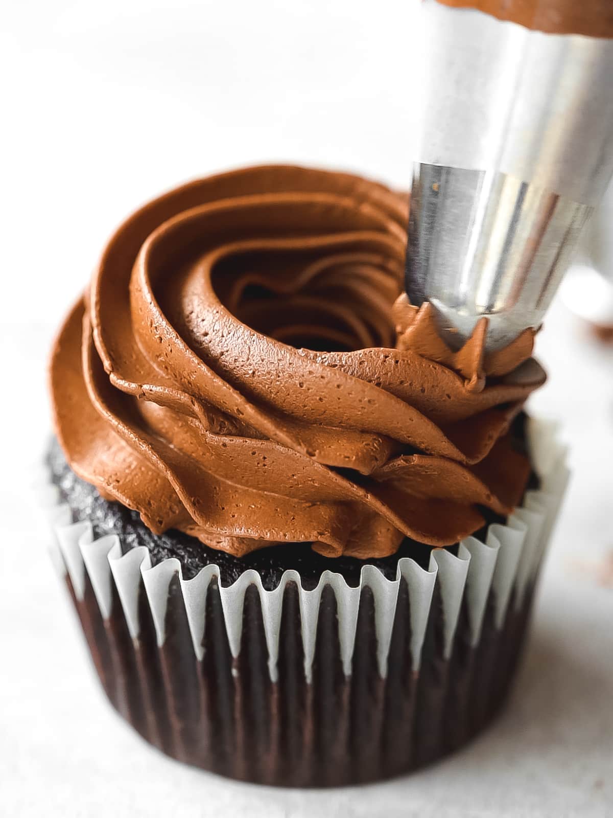 piping ganache frosting onto a chocolate cupcake.