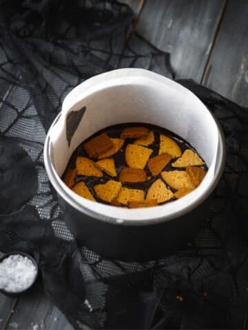 a lined cake pan with chopped biscuits and chocolate ganache.
