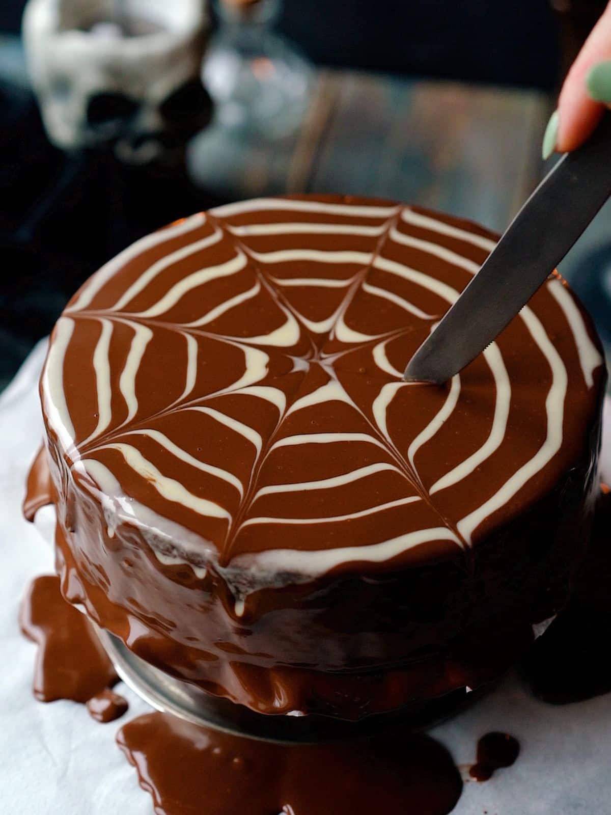 creating a spider web design on top of a chocolate cake with white chocolate and a knife.