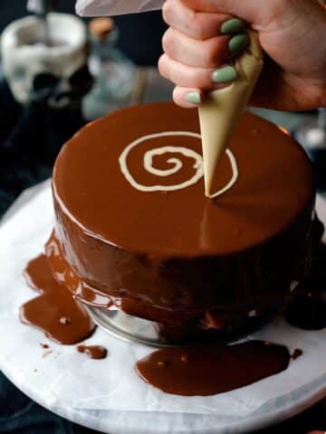 piping a spiral on top of a chocolate cake with white chocolate.