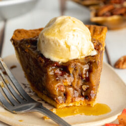 a slice of vegan pecan pie with a scoop of ice cream on top and a few bites taken from it showing the gooey filling.