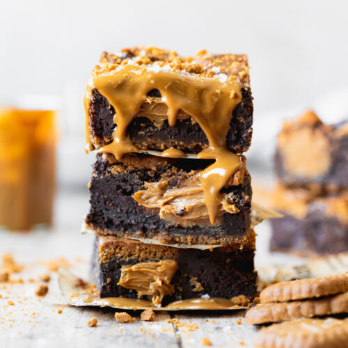 stack of biscoff brownies with cookie butter drizzled on top and lotus biscuits scattered around them.