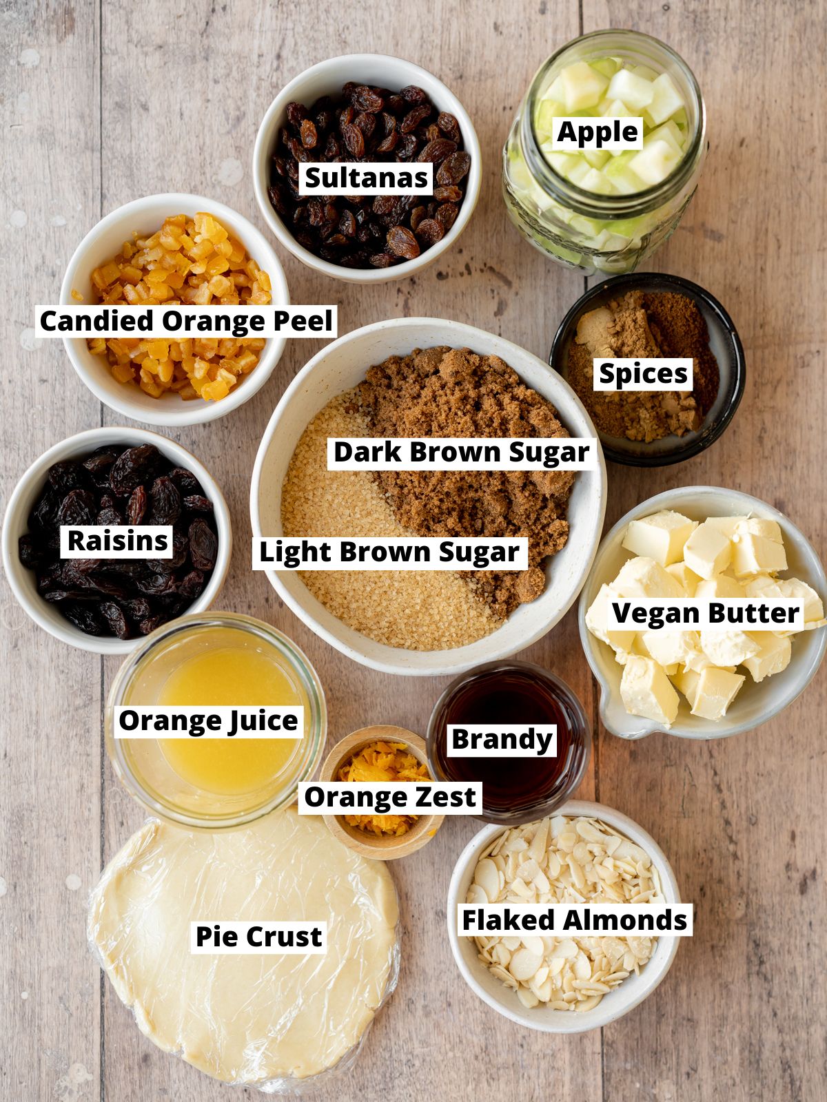 ingredients for homemade mince pies measured out in bowls on a wooden surface.