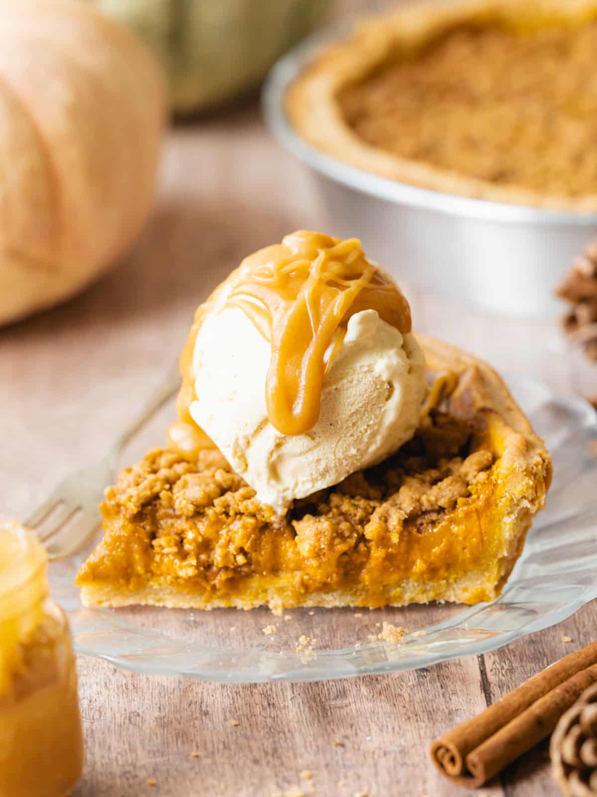 slice of pumpkin crumble pie with a a scoop of vanilla ice cream and butterscotch caramel on top.