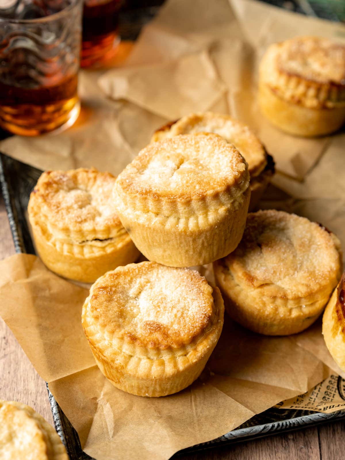 mince pies on a tray with a sheet of paper and 2 glasses of brandy in the background.