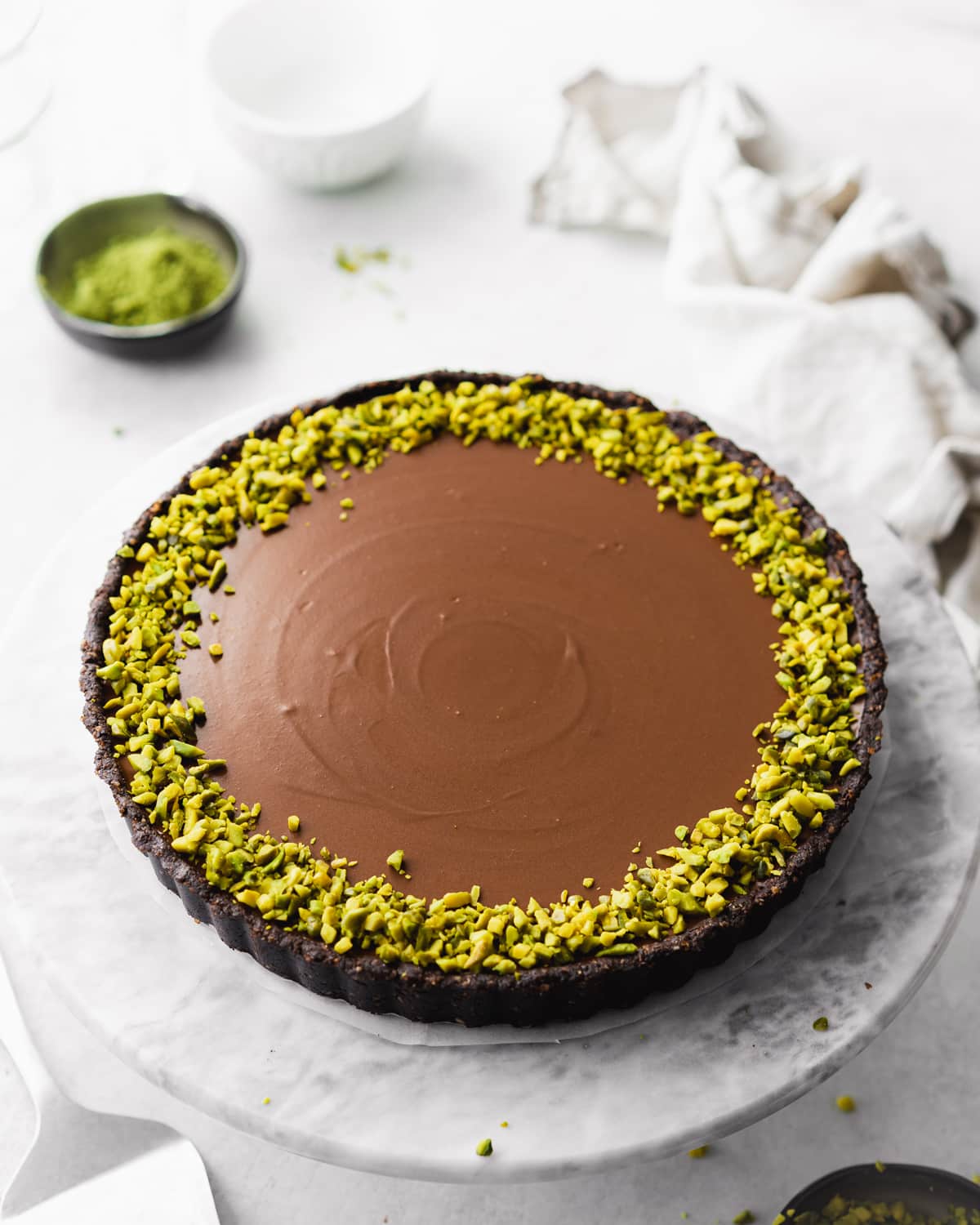 chocolate tart on a marble plate with pistachios on top.