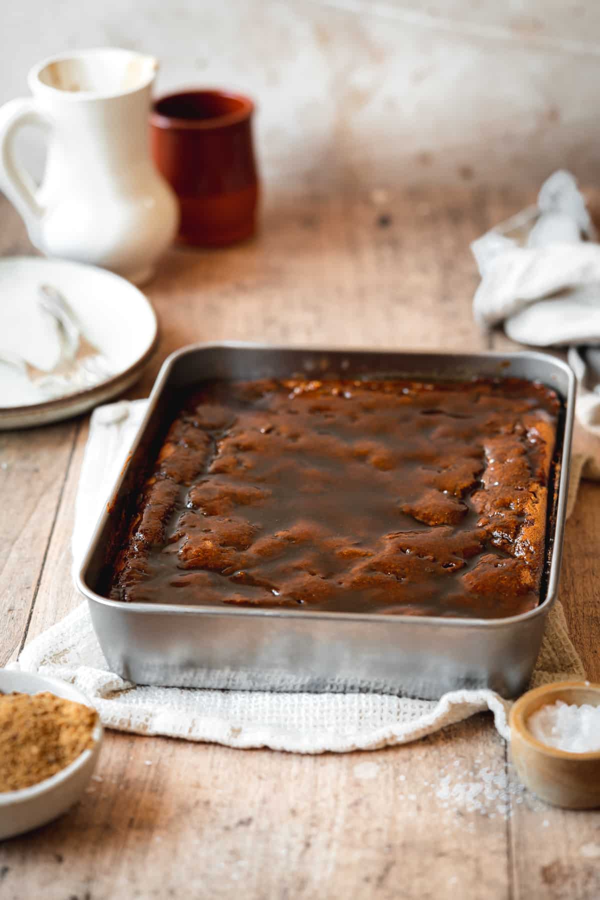 sticky toffee pudding in a rectangular metal pan on a wooden surface.
