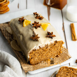 a loaf of sweet chai bread with orange segments, star anise, and icing on top of a rectangular plate.