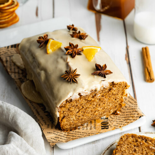 a loaf of sweet chai bread with orange segments, star anise, and icing on top of a rectangular plate.