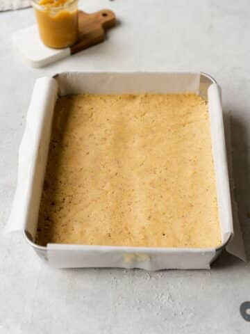 shortbread in a lined tray with holes pierced into it with a fork.