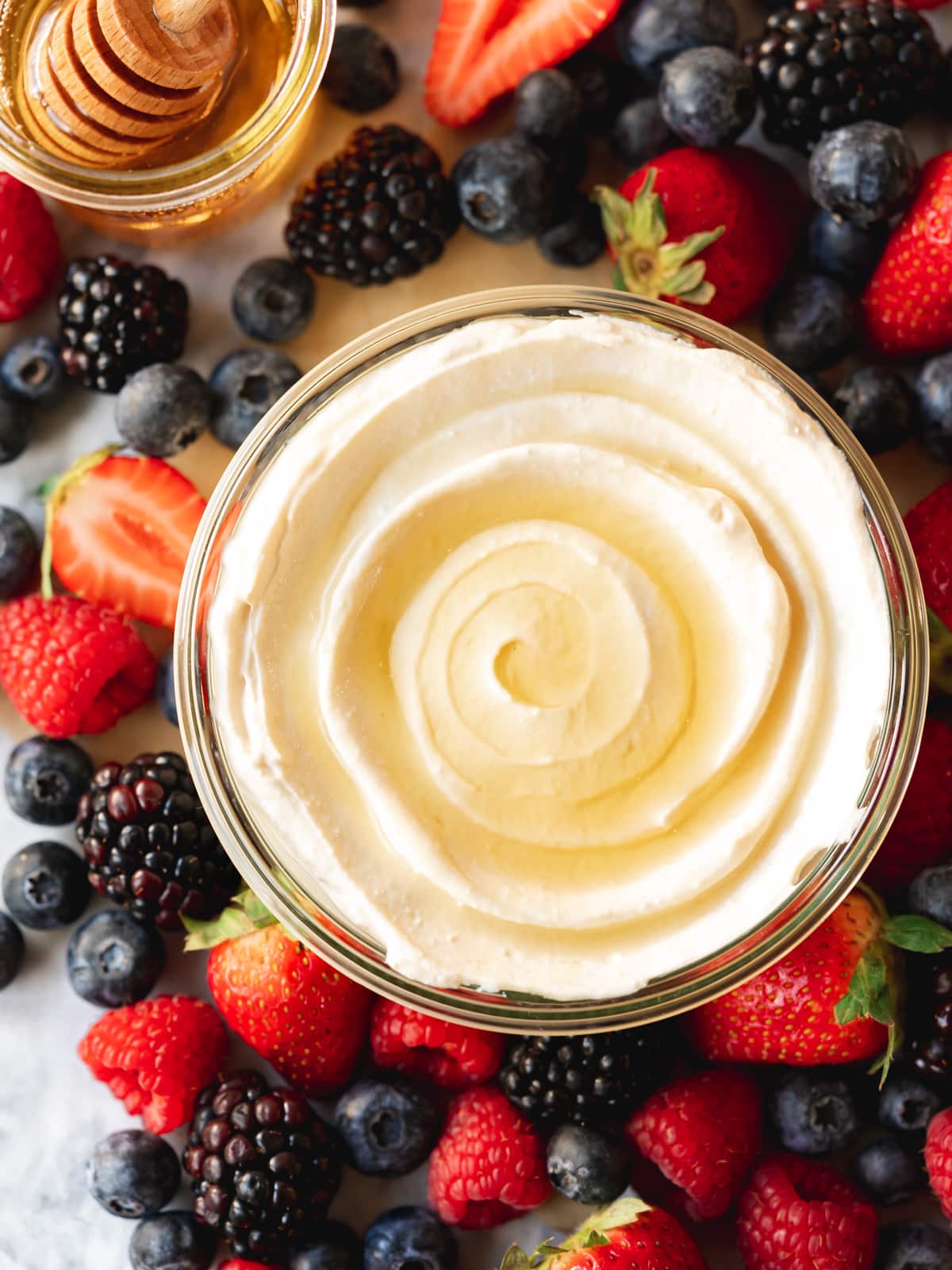 a glass pot of vegan mascarpone cheesecake with fresh berries and a pot of maple syrup in the background.