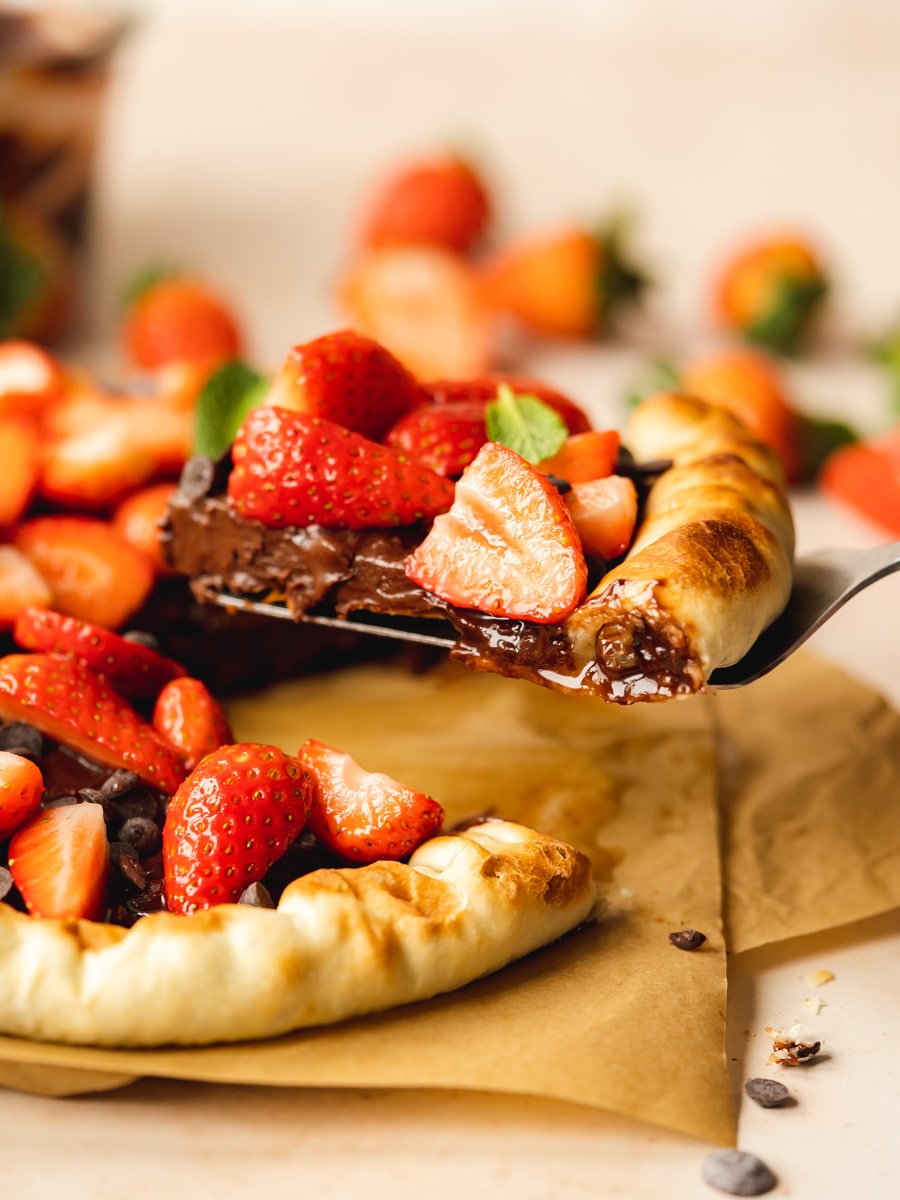 vegan chocolate pizza with strawberries on top with a slice being lifted off from it.