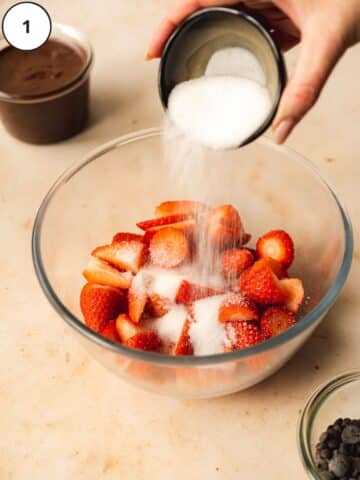 sprinkling sugar into a bowl of chopped strawberries.