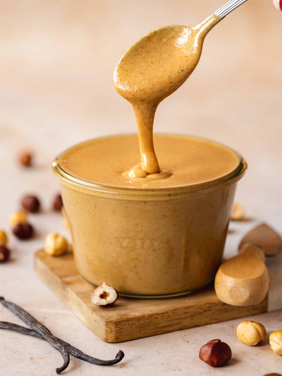 hazelnut butter in a jar with a spoon being dipped into it and vanilla pods next to it.