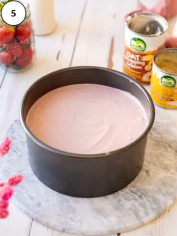 creamy vegan strawberry cheesecake in a cake tin on a marble surface.