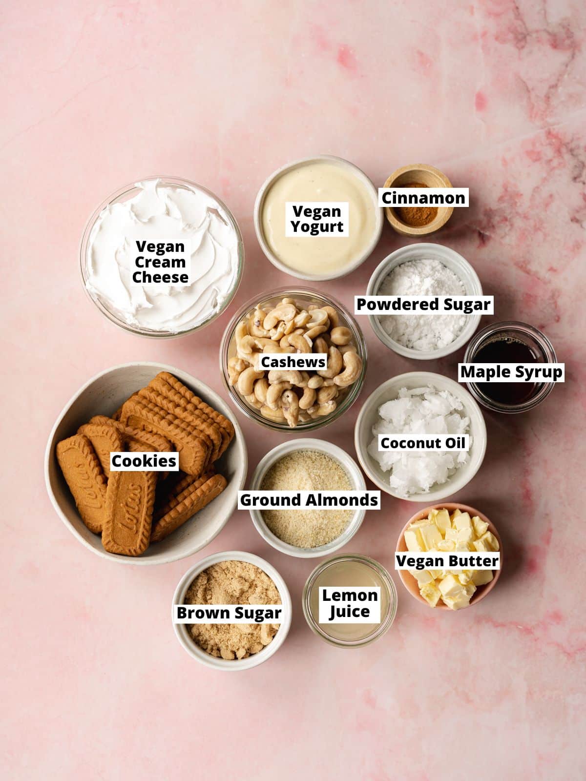 overhead shot of ingredients needed to make no-bake vegan cinnamon roll cheesecake measured out into bowls on a pink table with text overlay.