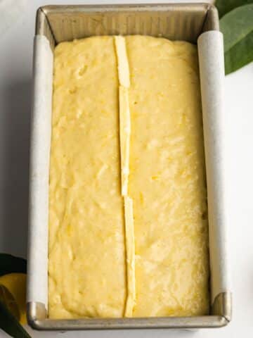 Vegan lemon loaf batter added to the prepared baking tin. Thin slices of vegan butter have been inserted in a line down the vertical middle of the pan.
