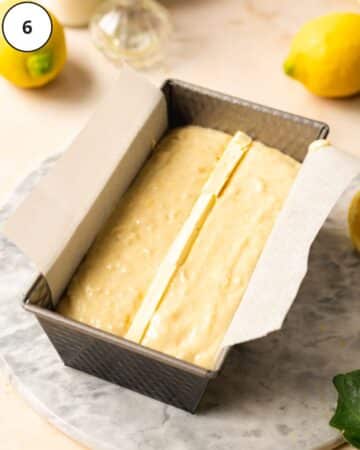 Vegan lemon loaf batter added to the prepared baking tin. Thin slices of vegan butter have been inserted in a line down the vertical middle of the pan.