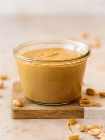 a weck jar filled with creamy peanut butter on a small wooden cutting board.